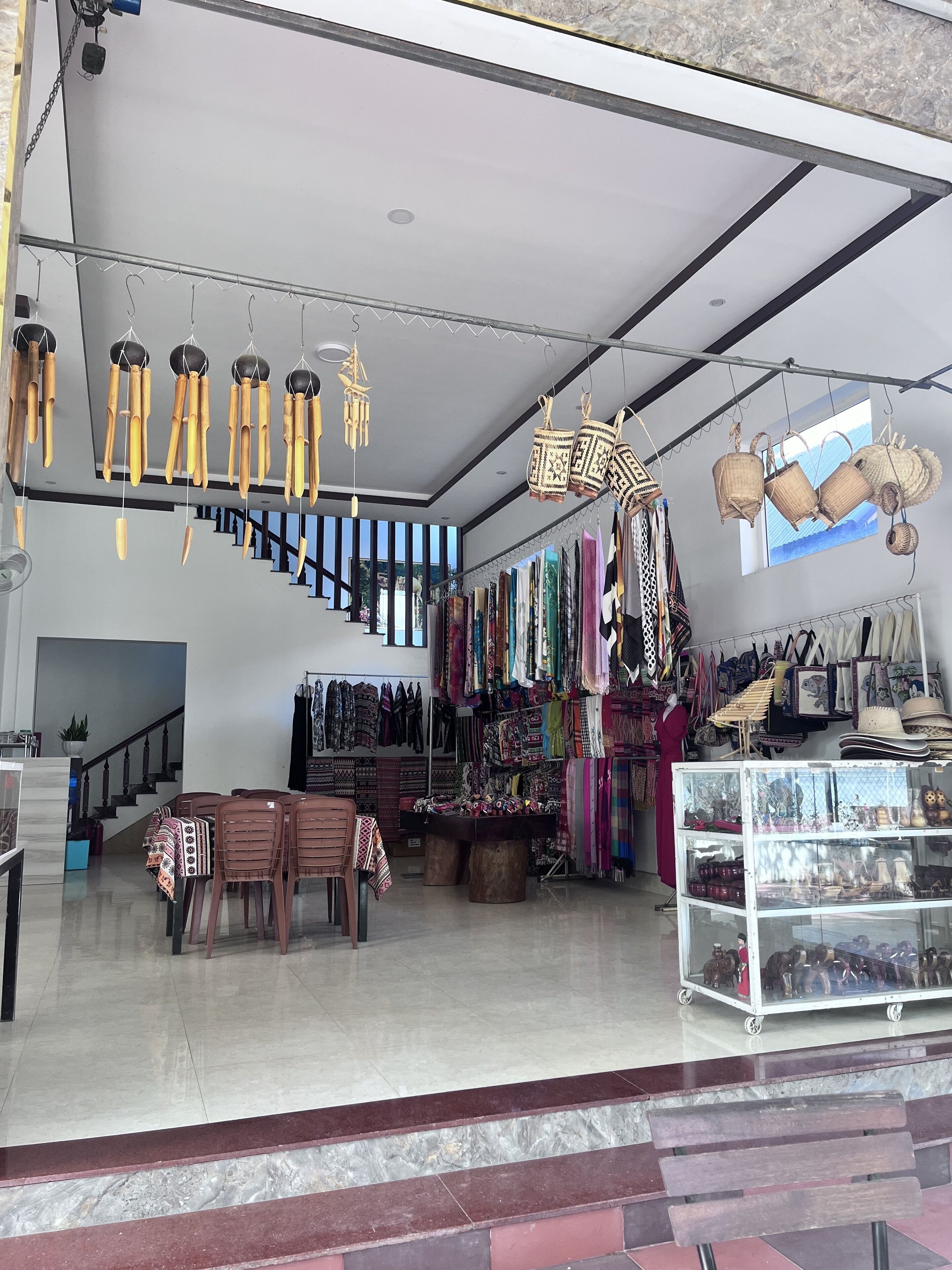 A spacious room with a staircase, a dining area with chairs and a table, and various hanging items like baskets and bags.