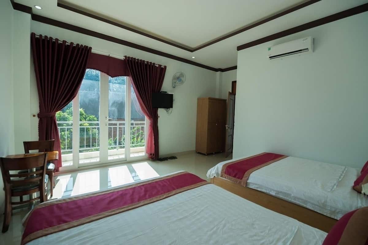 Quarto de hotel com duas camas, uma escrivaninha, uma cadeira, um guarda-roupa e varanda com cortinas.
