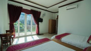 A hotel room with two beds, a desk, a chair, a wardrobe, and a balcony with curtains.