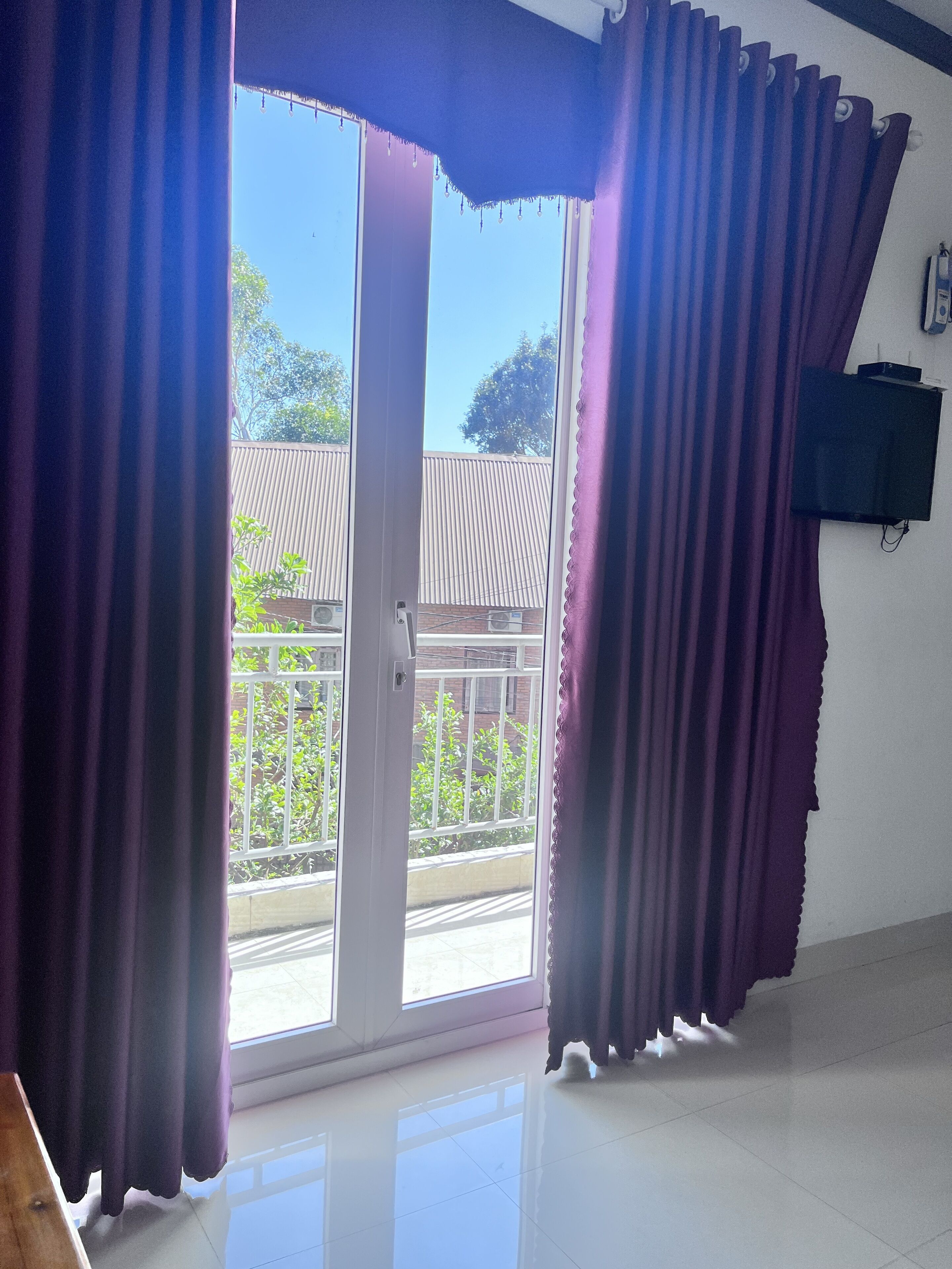 A room with a sliding glass door leading to a balcony, a flat-screen TV mounted on the wall, and a tiled floor.