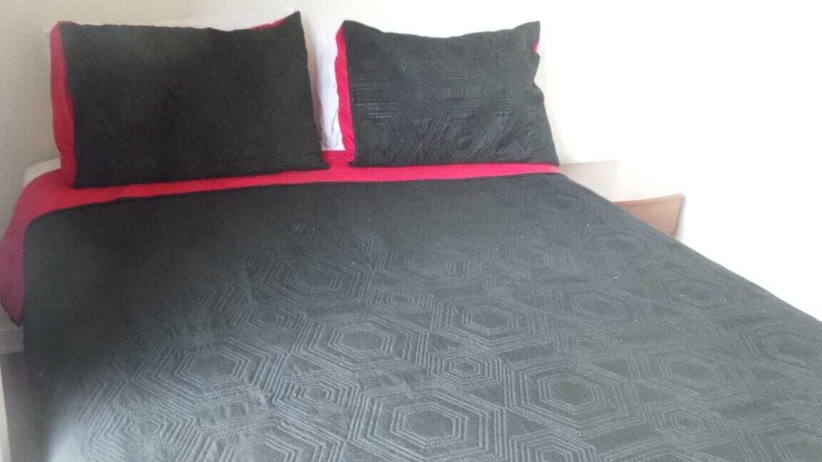 Een bed met een zwart-rood dekbed en twee zwarte kussens.