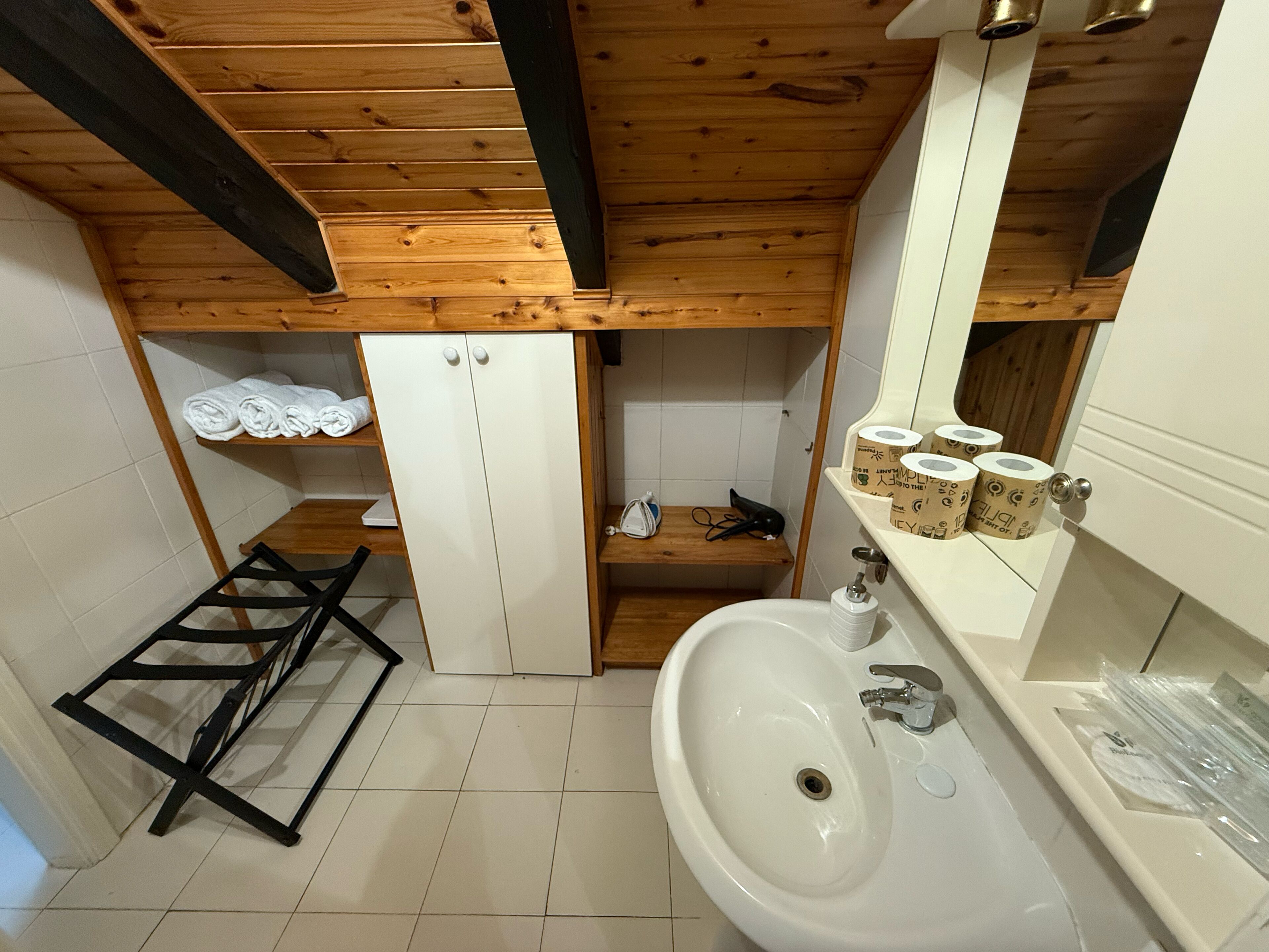 Ein Badezimmer mit Holzboden, weißen Fliesen und einem weißen Waschbecken sowie einem Spiegel.