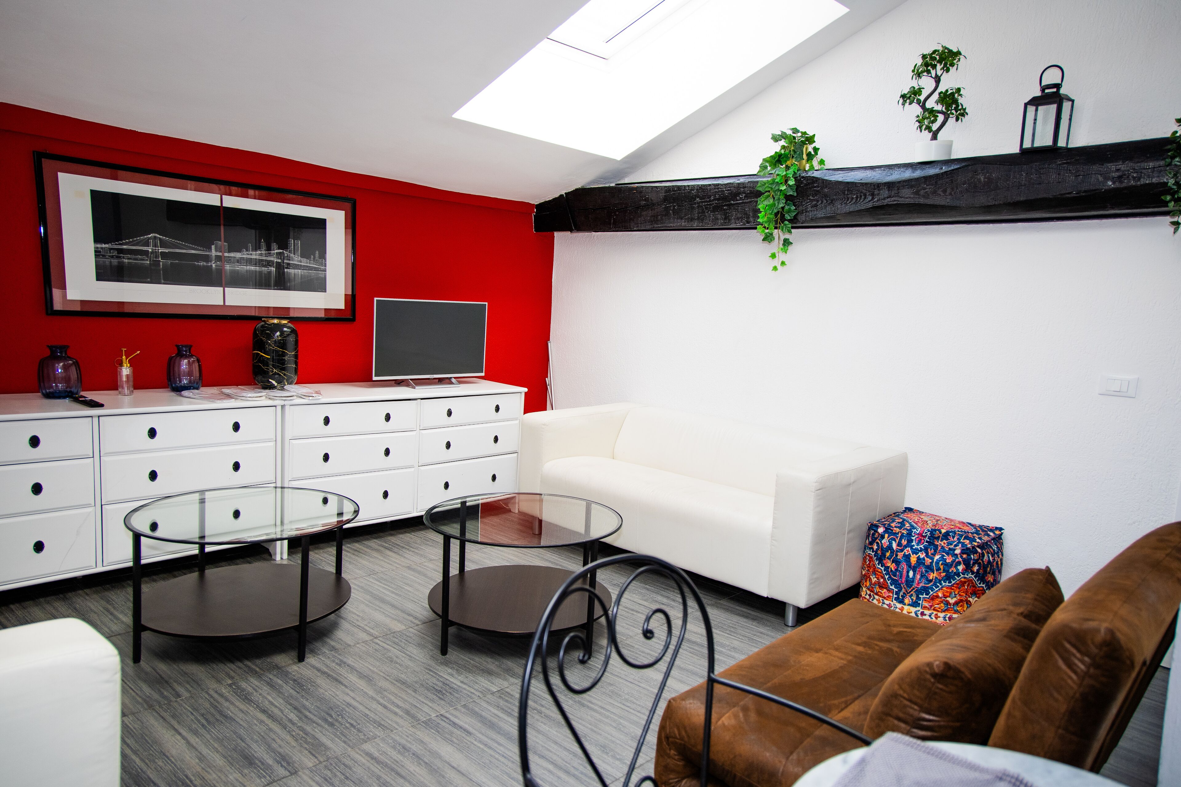 Uma sala de estar moderna com um sofá branco, duas mesas de centro de vidro, um sofá de couro marrom e uma parede com detalhes vermelhos.