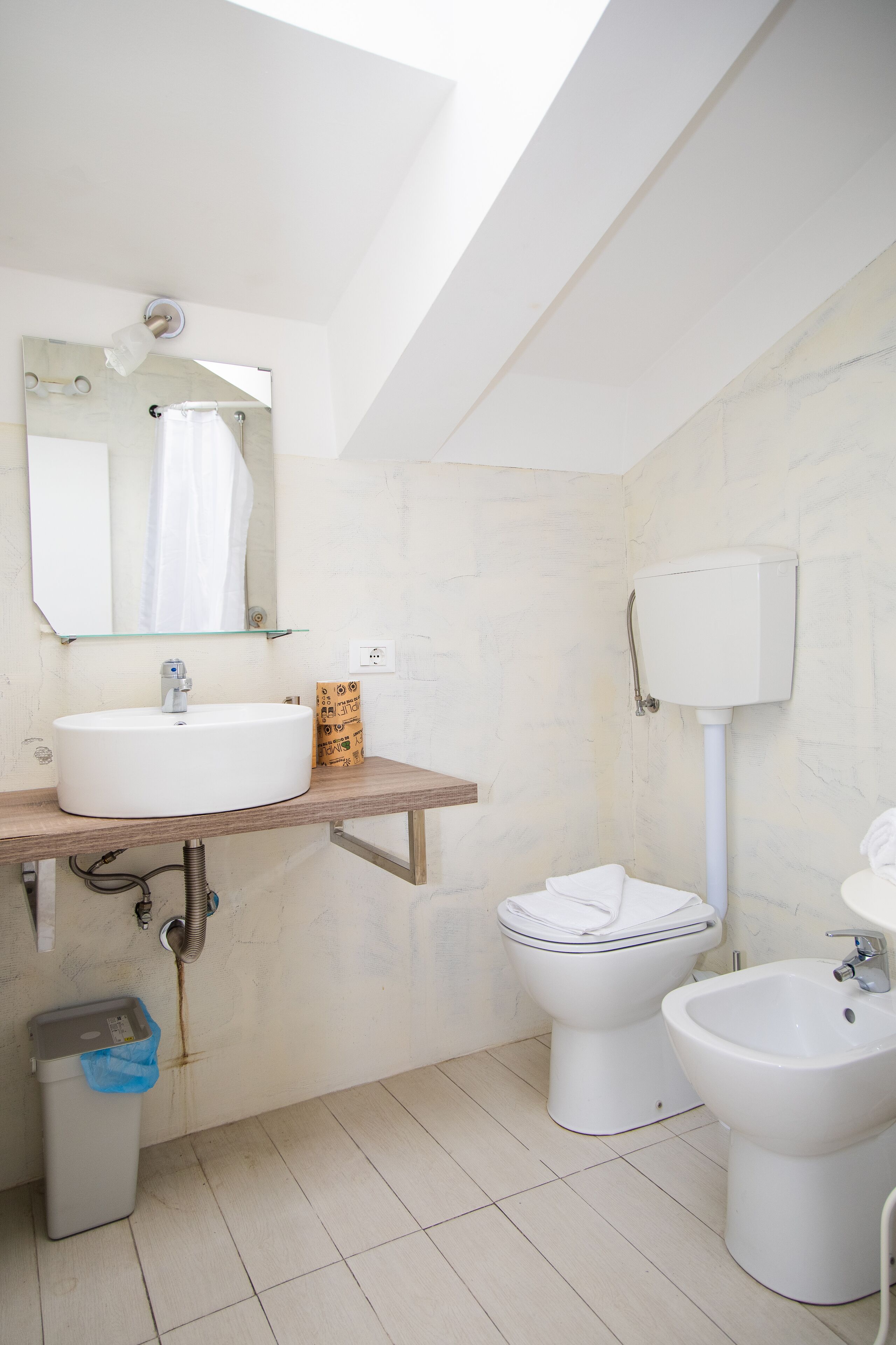 Een moderne badkamer met dakraam, wastafel, toilet, hygiëneschuimer en prullenbak.