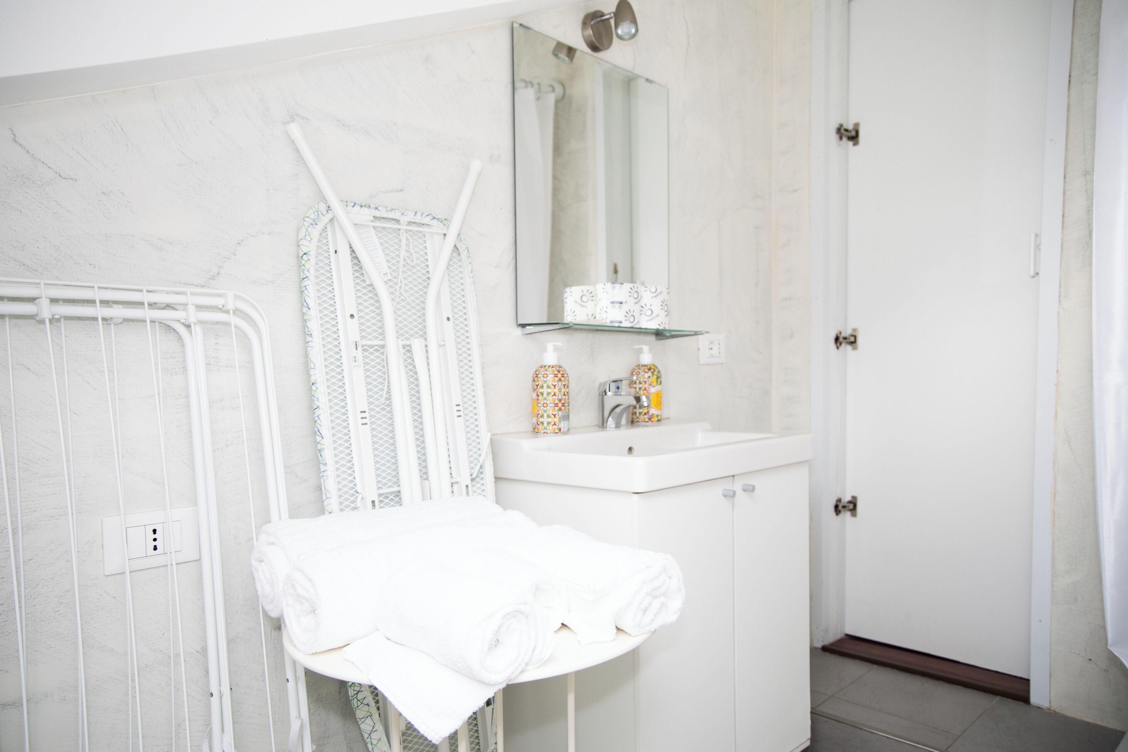 Un baño con lavamanos blanco, un espejo y un perchero para toallas.