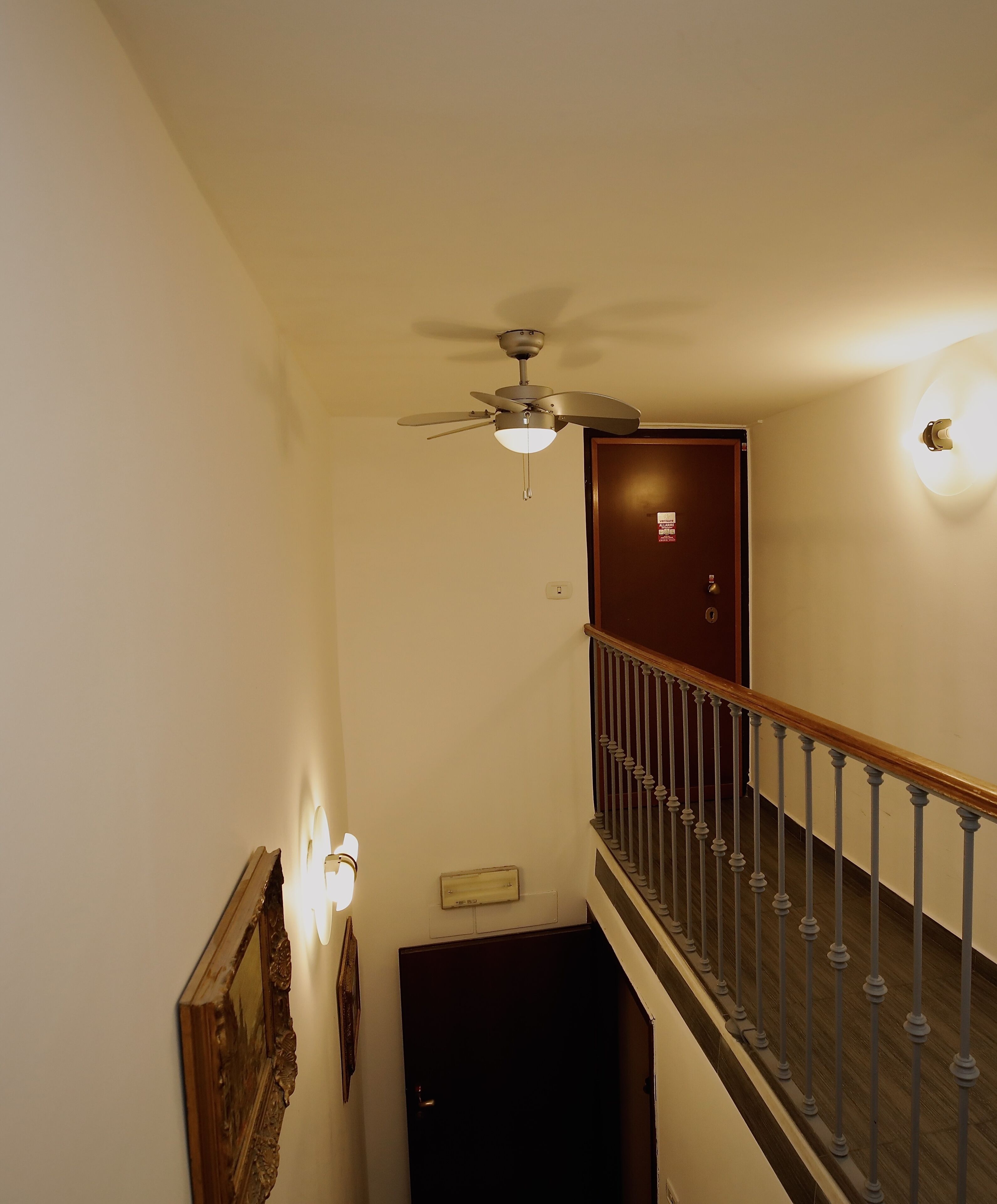 Eine Treppe mit Holzgeländer, einem Deckenventilator und einer Tür mit einem Schild.