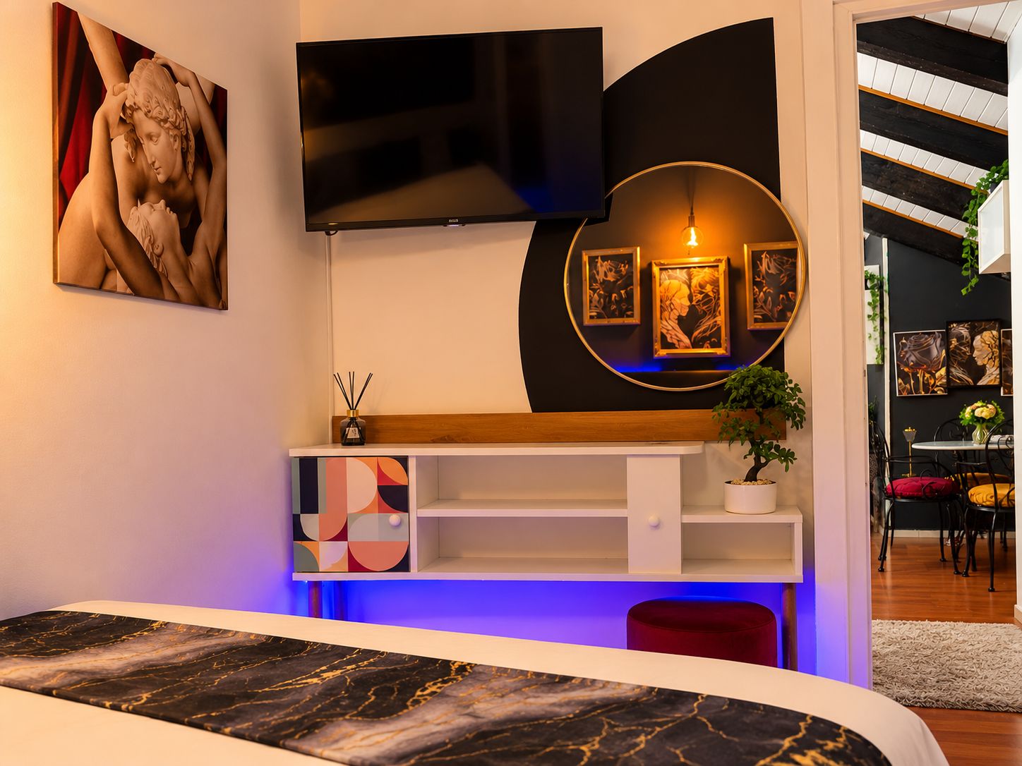 Un interior moderno con un televisor montado en la pared, una lámpara circular y una planta sobre una estantería.