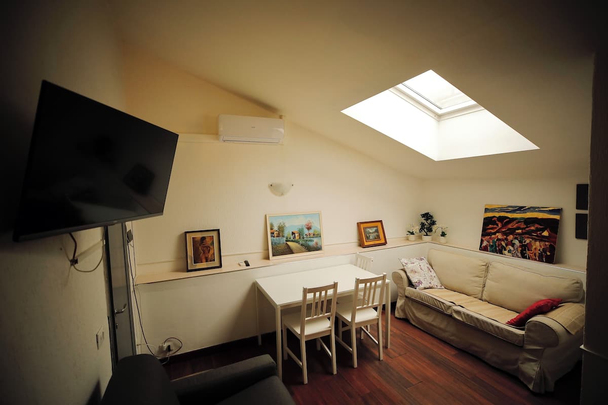 Um espaço de estar compacto com mesa de jantar, duas cadeiras, um sofá, televisão fixada na parede e um claraboia.