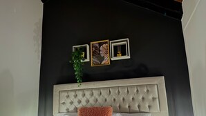 Ein Schlafzimmer mit einer gesteppten Kopfteil, einem weißen Bett mit zwei Kissen, einer kleinen Pflanze und zwei gerahmten Bildern an der Wand.