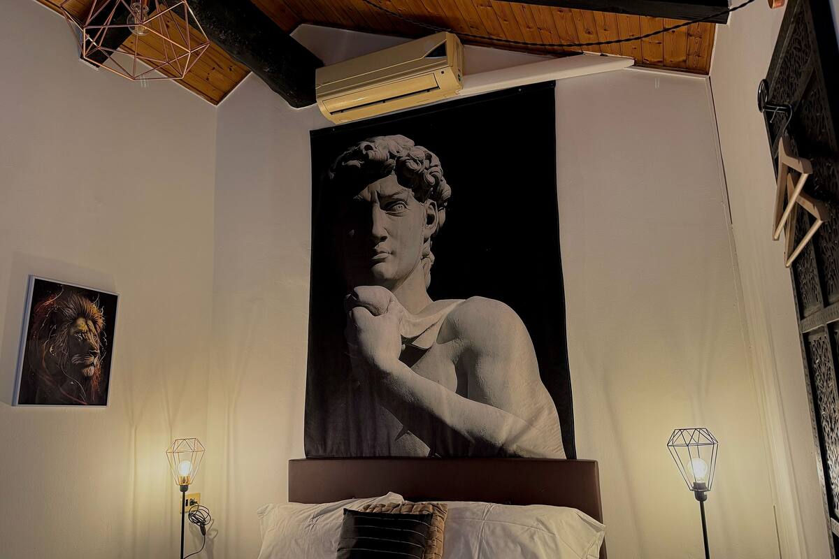 Um quarto com uma grande escultura na parede, uma cama com cabeceira e duas luminárias de chão.