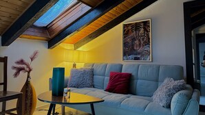 Ein modernes Wohnzimmer mit hoher Decke, Holzbalken, einem Oberlicht, einer Couch mit Kissen, einem kleinen Tisch, einer dekorativen Vase und einem gerahmten Tigerbild.