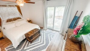 Une chambre à coucher comprenant un lit, un ventilateur de plafond, une table de chevet, une fenêtre avec des rideaux et une vue sur l’extérieur.