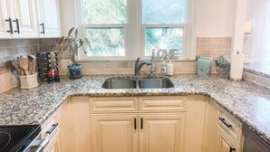Une cuisine avec deux fenêtres, un plan de travail en granit et des meubles de couleur beige.