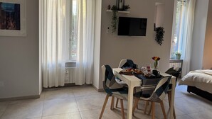 Una habitación con una mesa de comedor, sillas, una cama, un televisor y un ventanal con cortinas.
