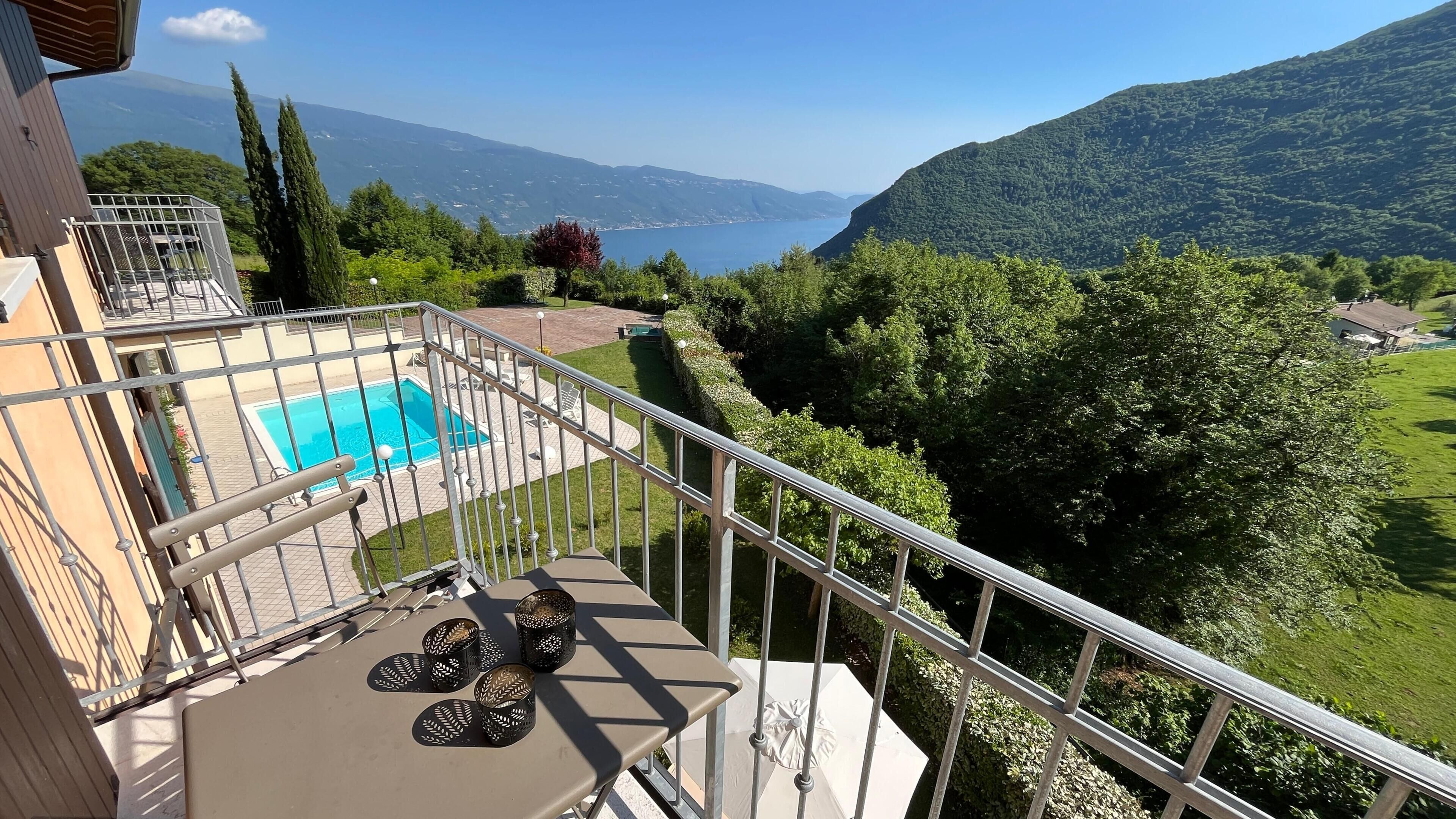 Ein Balkon mit Pool, Gartenmöbeln und Blick auf einen See und Berge.