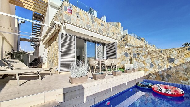 Ein modernes Haus mit Naturstein-Fassade, einem Pool, Gartenmöbeln und blauem Himmel.