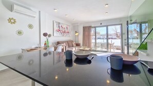 Eine moderne Küche mit einer großen schwarzen Arbeitsplatte, einem Essbereich mit Tisch und Stühlen, einer Couch und einem großen Fenster mit Blick ins Freie.