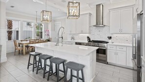 A modern kitchen with white cabinetry, a large island with bar stools, stainless steel appliances, and pendant lighting. - Pool ~ Walk to Beach ~ 2 Balconies (Inlet Beach)