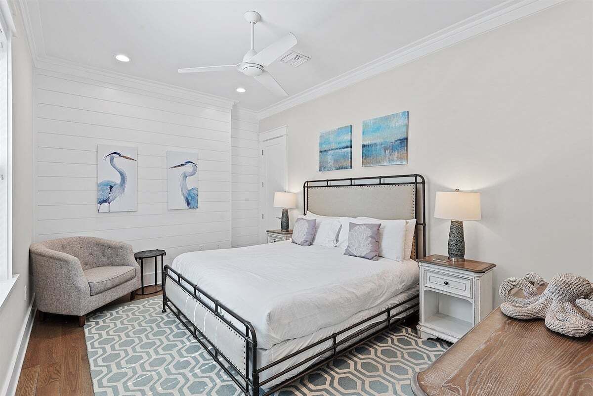 Une chambre à coucher comprenant un lit, deux tables de chevet, une chaise, un ventilateur de plafond et des œuvres d’art murales.