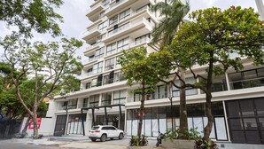 Un immeuble à plusieurs étages doté de balcons, une voiture garée devant et des arbres au premier plan.