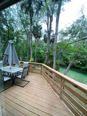 A wooden deck with a table and chairs, surrounded by tall trees and a body of water. -  Weeki Wachee river !! REAL FLORIDA! Read OUR  5 STAR REVIEWS (Spring Hill)