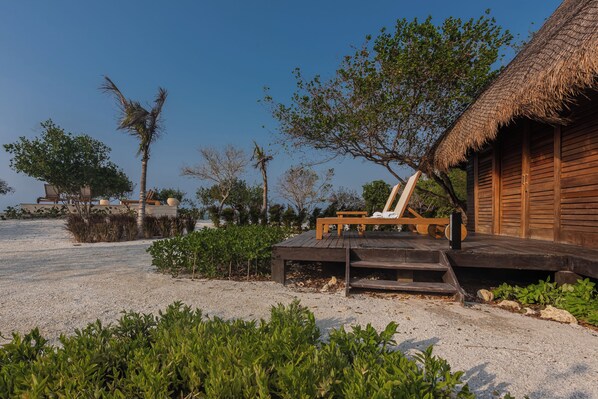 Une structure en bois située au bord de la plage, avec un toit de chaume, une terrasse en bois et un fauteuil de relaxation.