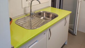 Une cuisine de taille réduite, dotée d’un évier en acier inoxydable, d’un plan de travail vert et de meubles blancs.