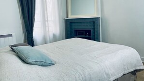 A bedroom with a bed, a blue pillow, a white blanket, a blue fireplace, and a large mirror on the wall.
