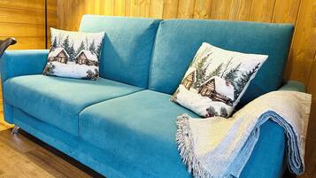 Un sofá color turquesa con dos almohadones decorativos y una manta, sobre piso de madera.