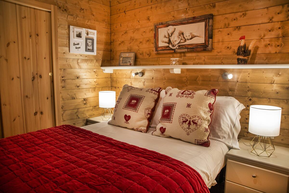 Ein Zimmer mit Holzwandverkleidung, einem Bett, zwei Nachttischlampen, einem Nachttisch und einem Regal mit Dekoration.