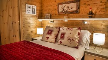 Quarto com painéis de madeira, uma cama, duas luminárias de cabeceira, uma mesinha de cabeceira e uma estante com objetos decorativos.
