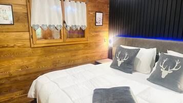A wooden-paneled room with a bed, two windows with curtains, and a headboard with a light strip.
