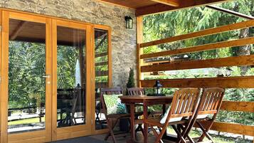 A covered patio with a stone wall, wooden ceiling, and a table with chairs.