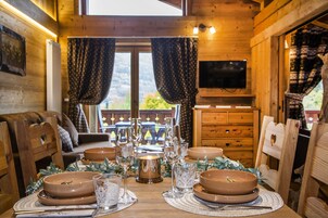 A wooden cabin interior with a dining table set for a meal, surrounded by wooden chairs.