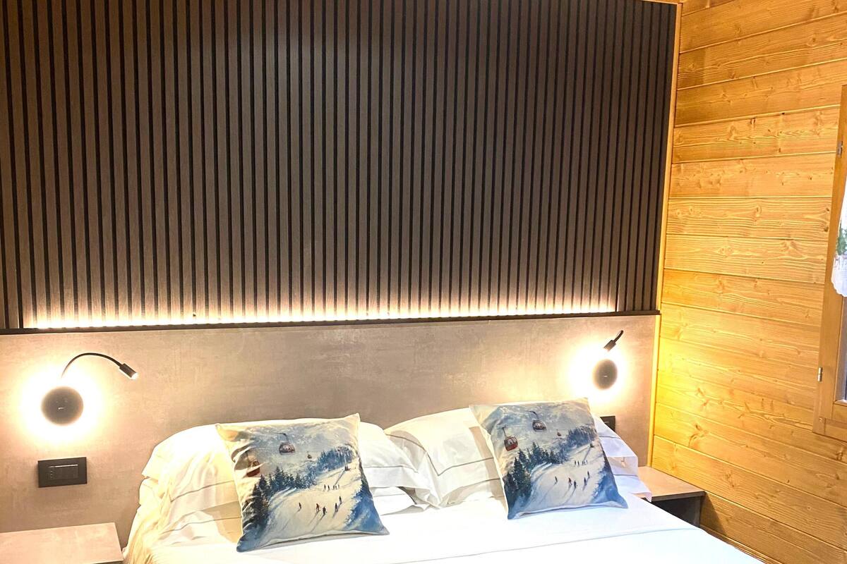 Ein Schlafzimmer mit Holzboden, einem Bett mit weißer Bettwäsche, zwei Kissen mit Bergmotiven und zwei Nachttischlampen.