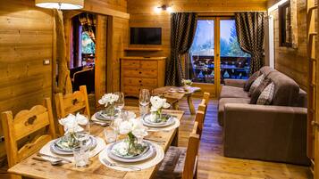 A wooden interior with a dining table set for four, a sofa, and a TV mounted on the wall.