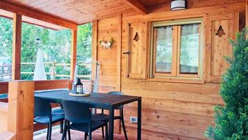 Eine Holzhütte mit Tisch und Stühlen, ein Fenster mit Fensterläden und ein kleiner Baum.