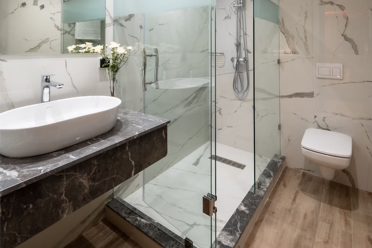 A modern bathroom with a glass-enclosed shower, a marble vanity, and a white toilet.