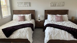 Een slaapkamer met twee bedden, elk met een houten hoofdbord, witte beddengoed en een donkere plaid. Er zijn twee nachtkastjes met lampen, en kunstwerken aan de wanden.
