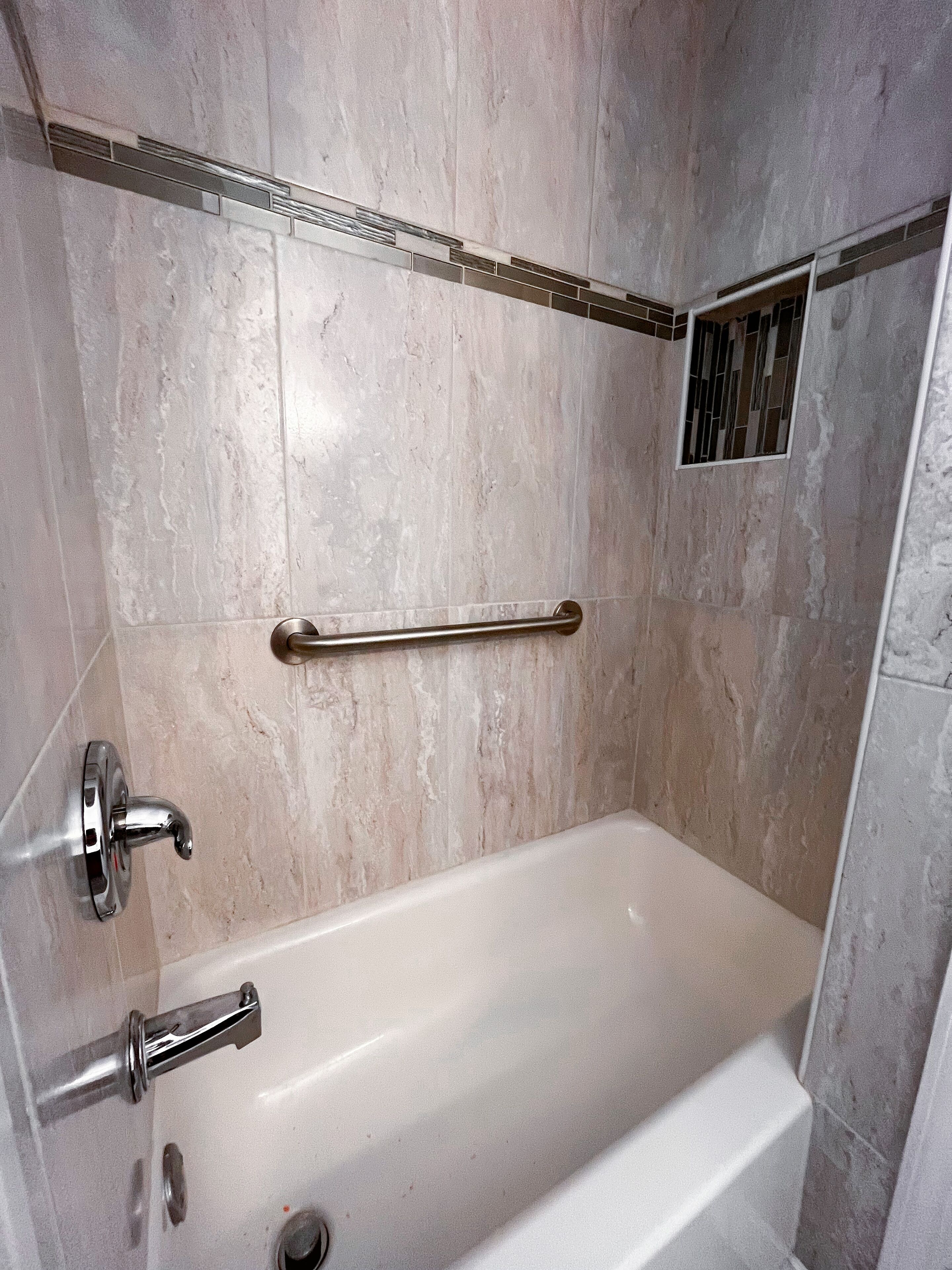 A bathroom with a bathtub, a handrail, and a showerhead.