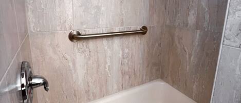 A bathroom with a bathtub, a handrail, and a showerhead.