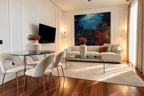 Un salon moderne avec une table basse en verre, des canapés blancs et un grand tableau abstrait.