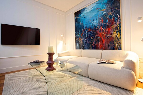 Un salon moderne avec un grand tableau abstrait, un téléviseur à écran plat et une table basse en verre.