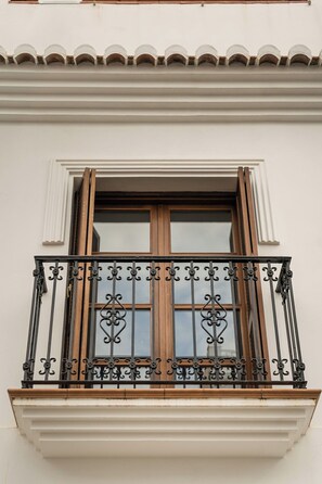 A building facade with a window, a balcony with ornate black metal railings, and a white trim around the window.