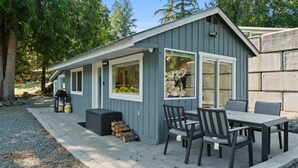 A small, single-story building with a patio area, a table and chairs, and a barbecue grill.