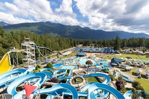 A water park with multiple slides and pools, surrounded by mountains and trees.