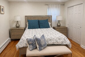 A bedroom with a bed, two bedside tables, a bench, a window with curtains, and a door.