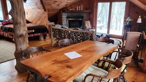 Een rustiek houten interieur met een eettafel, stoelen, een open haard en een gezellige zithoek.