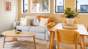 Un salon comprenant un canapé, une table basse et une table à manger avec des chaises. Des œuvres d’art encadrées ornent le mur, et une plante en pot est posée sur la table.