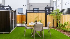 Une petite terrasse extérieure avec une table et des chaises, entourée d’une clôture en bois et d’un portail noir.